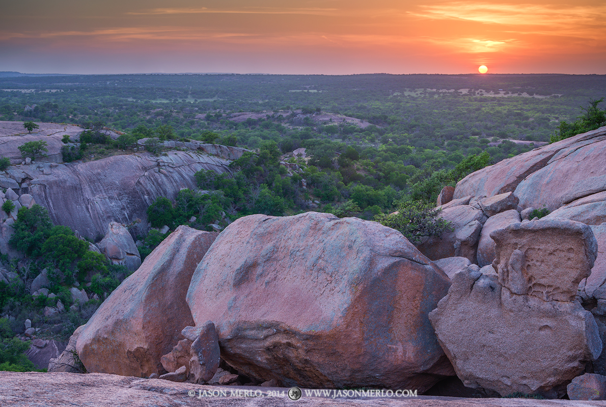 The sun appears as an orange ball on the horizon at sunset at Enchanted Rock State Natural Area in Llano County in the Texas...