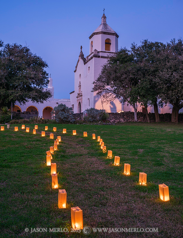 Christmas luminarias and lights adorn the mission grounds at night at Mission Nuestra Señora del Espíritu Santo de Zúñiga...